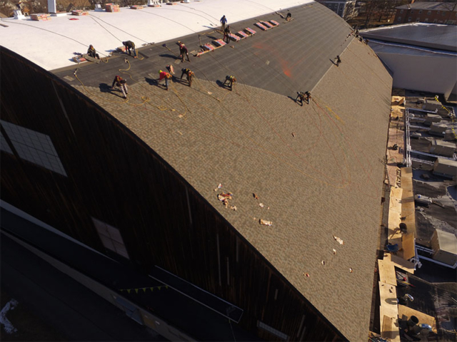 roofers installing shingles on a large commercial arched roof