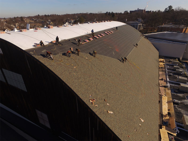 roofers installing shingles on a large commercial arched roof