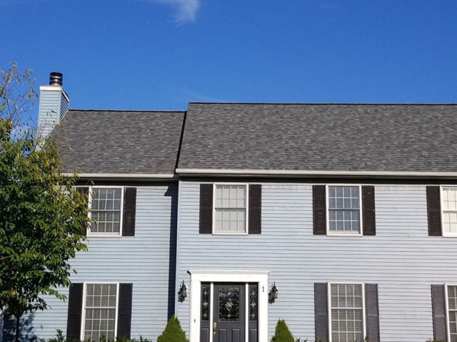 New roof of multi-shade gray shingles on a light blue home.