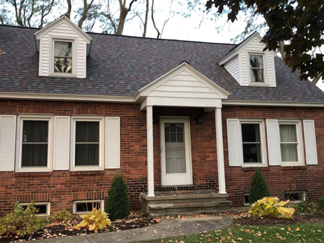 Multicolored shingle replacement roof on a brick home with white pillars and trim