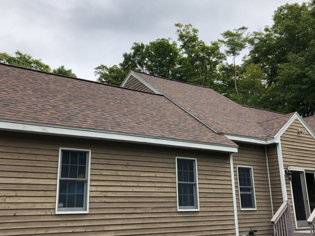replacement roof with brown shingles on a wood sided home