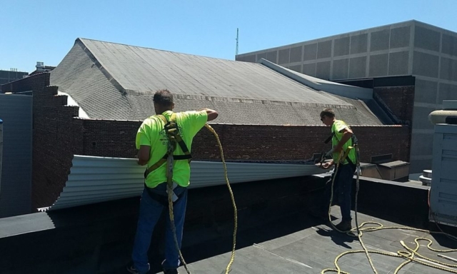 Two workers in safety harnesses on a flat roof