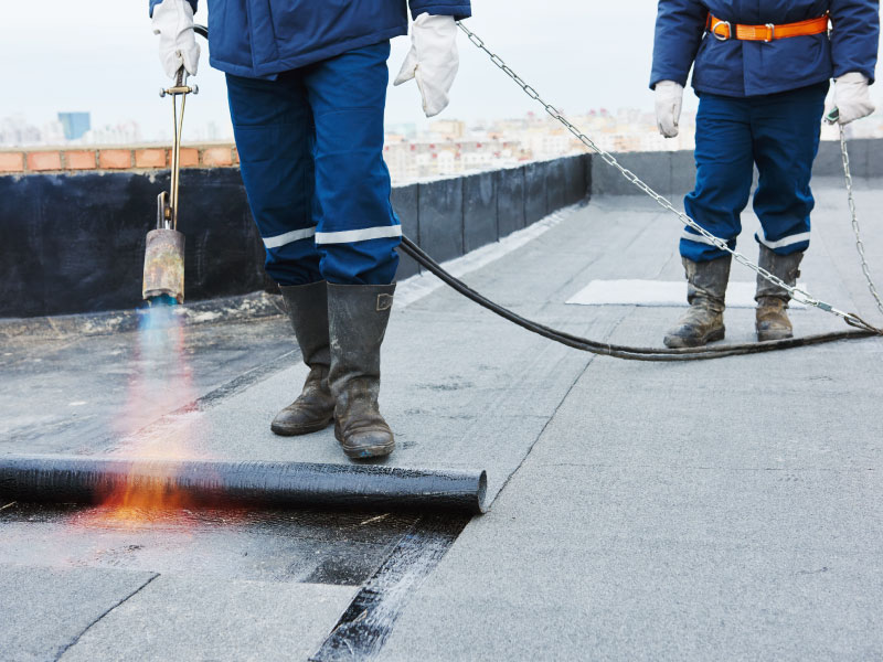 Workers applying bitumen roofing